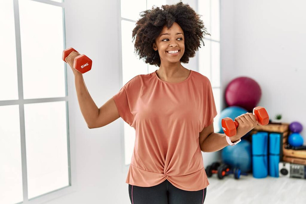 Fiatal afro-amerikai nő mosolygós magabiztos edzés segítségével súlyzók sportközpontban - Fotó, kép