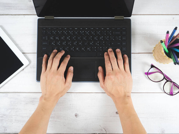 Рука на клавиатуре ноутбука с очками и мобильно на столе вид сверху - Фото, изображение