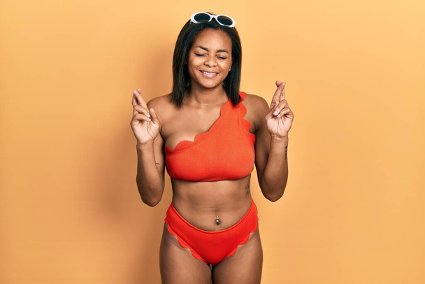 Young african american girl wearing bikini gesturing finger crossed smiling with hope and eyes closed. luck and superstitious concept.  - Фото, изображение