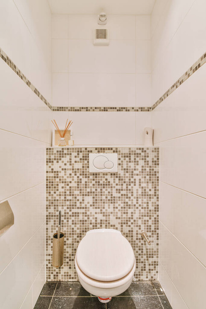 A modern toilet is installed on the wall under a button and a shelf with a diffuser in a light restroom at home - Photo, Image