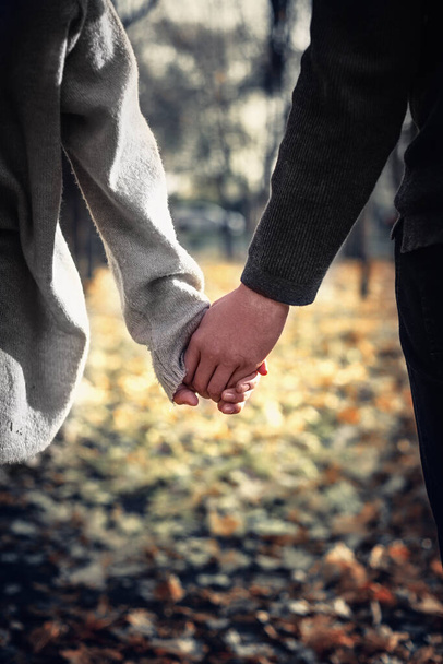 Zbliżenie zakochanej pary trzymającej się za ręce podczas spaceru. Skupienie selektywne, pionowe. - Zdjęcie, obraz
