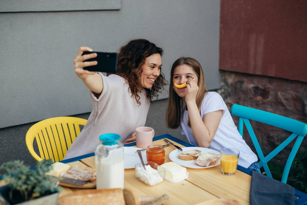 mother and daughter taking selfie with smartphone while eating breakfast at home - Фото, зображення