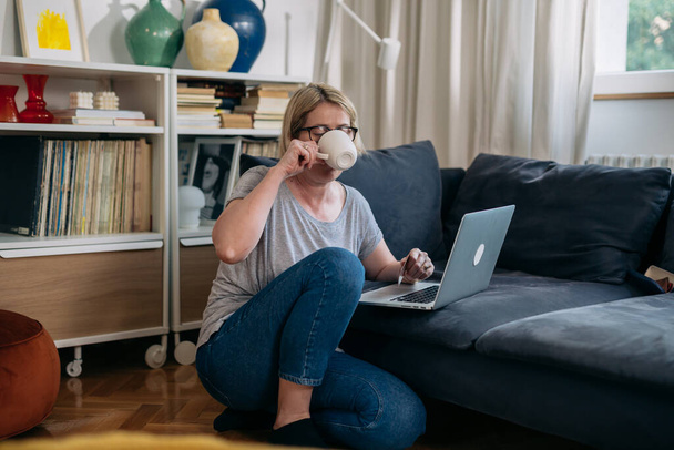 mature woman using laptop computer in her living room - Photo, Image
