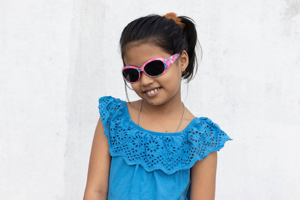 Uma menina indiana usando óculos de sol olhando para a câmera com rosto sorridente no verão no fundo branco - Foto, Imagem