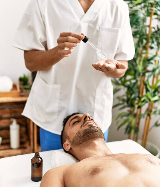 Zwei hispanische Männer Therapeut und Patient mit Gesichtsbehandlung mit Serum im Schönheitszentrum - Foto, Bild