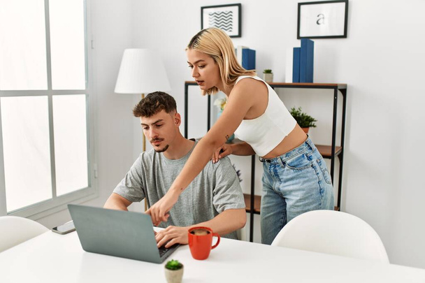 Молода біла пара використовує ноутбук і п'є каву, сидячи на столі вдома
. - Фото, зображення