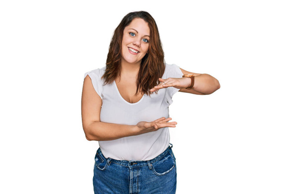 Young plus size woman wearing casual white t shirt gesturing with hands showing big and large size sign, measure symbol. smiling looking at the camera. measuring concept.  - Photo, Image