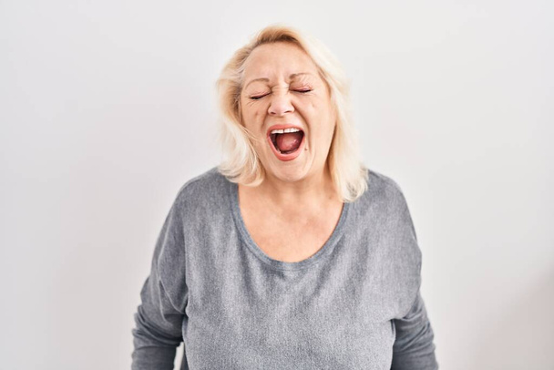 Middle age caucasian woman standing over white background angry and mad screaming frustrated and furious, shouting with anger. rage and aggressive concept.  - Foto, Imagen