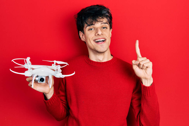 Bonito jovem hipster segurando drone sorrindo com uma ideia ou pergunta apontando dedo com cara feliz, número um  - Foto, Imagem