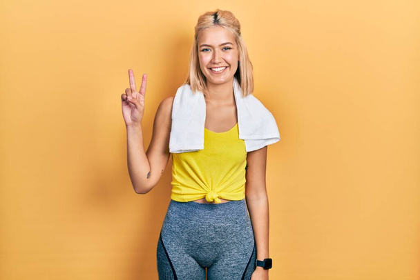 Belle femme sportive blonde portant tenue d'entraînement montrant et pointant vers le haut avec les doigts numéro deux tout en souriant confiant et heureux.  - Photo, image