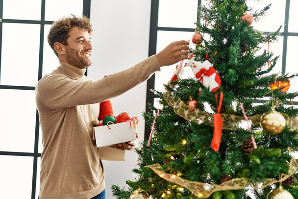 Genç İspanyol adam gülümsüyor. Evde kendine güvenen bir Noel ağacı süslüyordu. - Fotoğraf, Görsel