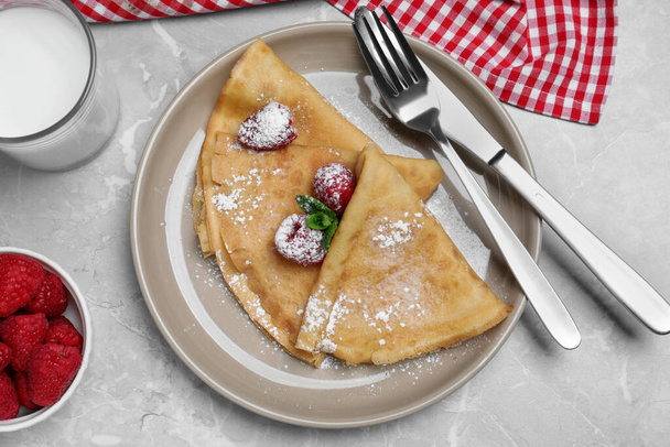 Delicious crepes served with mint, raspberries, powdered sugar and glass of milk on grey table, flat lay - Foto, Imagem