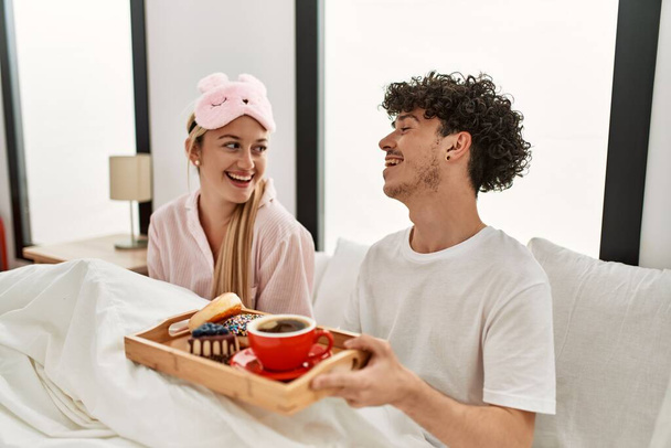 Junges schönes Paar lächelt glücklich beim Frühstück auf dem Bett zu Hause. - Foto, Bild