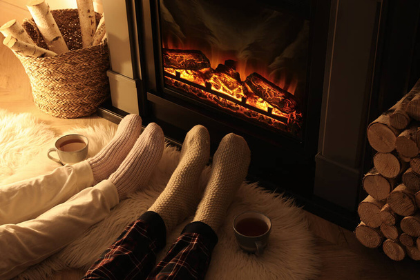 Couple in knitted socks near fireplace at home, closeup of legs - Foto, afbeelding