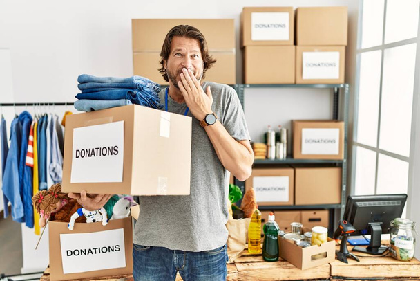 Pohledný muž středního věku drží dárcovskou krabici pro charitu na dobrovolníka stojí se smíchem a rozpačitě se hihňá zakrývající ústa rukama, drby a skandálním pojetím  - Fotografie, Obrázek