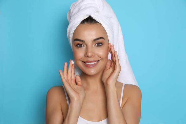 Beautiful young woman with towel applying cream on face against light blue background - Fotografie, Obrázek