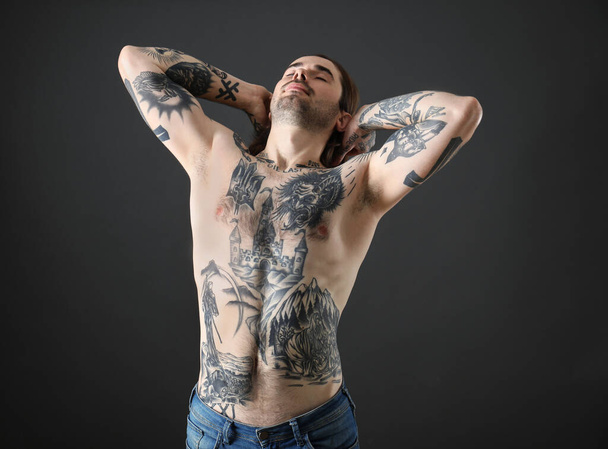 Junger Mann mit Tätowierungen am Körper vor schwarzem Hintergrund - Foto, Bild