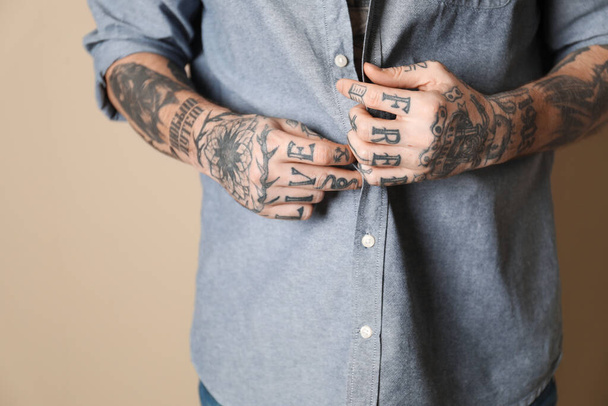 Young man with tattoos on body against beige background, closeup - Фото, изображение