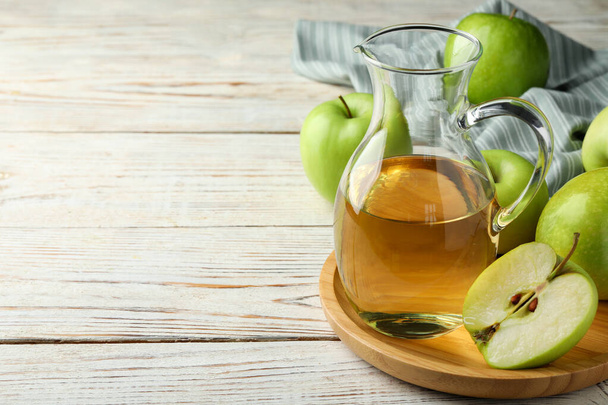 Dzbanek smacznego soku i świeżo dojrzałe zielone jabłka na białym drewnianym stole, miejsce na tekst - Zdjęcie, obraz