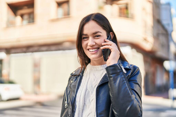 jonge vrouw glimlachen zelfverzekerd praten op de smartphone op straat - Foto, afbeelding