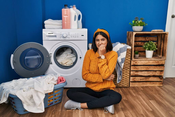 Young hispanic woman doing laundry looking stressed and nervous with hands on mouth biting nails. anxiety problem.  - Fotoğraf, Görsel