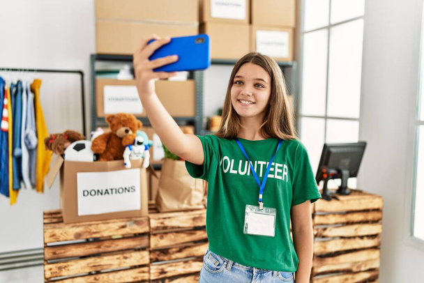 Suloinen tyttö yllään vapaaehtoinen univormu tehdä selfie älypuhelimen hyväntekeväisyyskeskuksessa - Valokuva, kuva