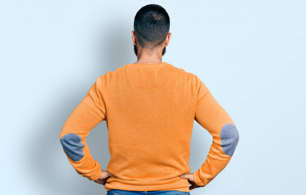 Hispánec s vousy na sobě ležérní zimní svetr stojí pozpátku dívá pryč s rukama na těle  - Fotografie, Obrázek