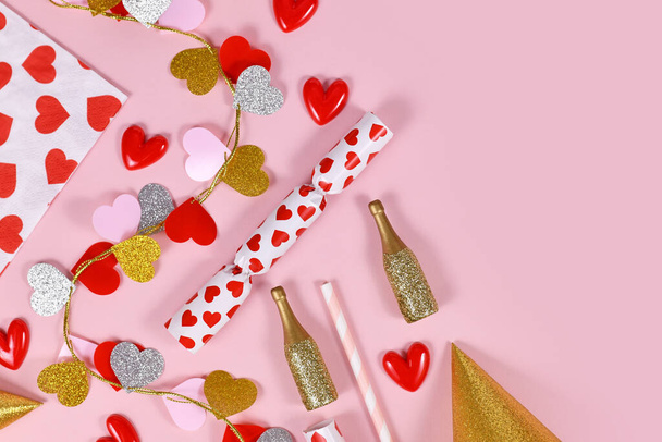 Party flat lay with heart garland, napkin, champagne bottles and party hats on pink background - Photo, Image
