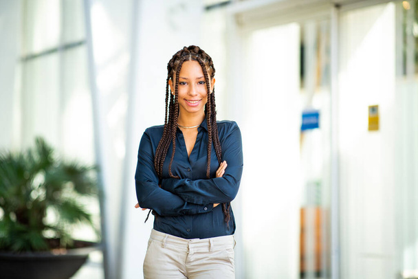 Portrait of smiling young black woman standing outdoors with her arms crossed and looking at camera - Photo, Image