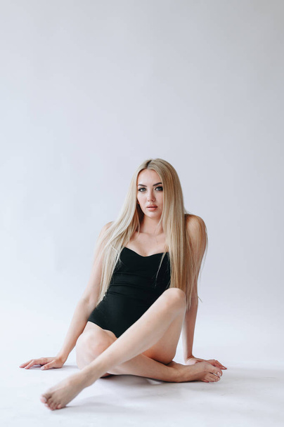 Girls with long hair sit cross-legged in a black bodysuit on a white background. ecological sign. Ecology concept. copy space - Fotografie, Obrázek