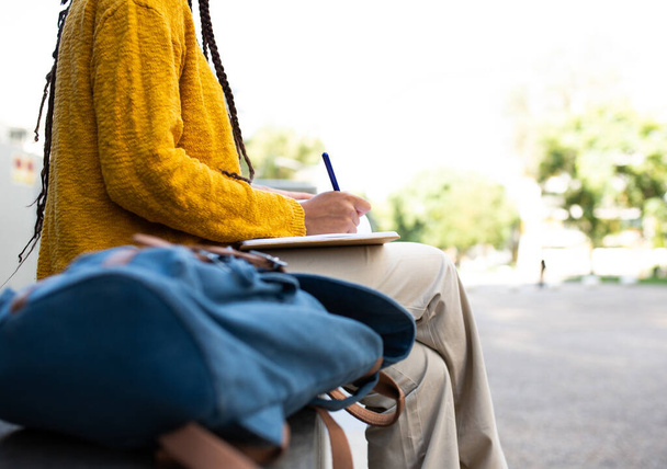 Close up retrato de estudante africana sentada do lado de fora escrevendo em um livro - Foto, Imagem