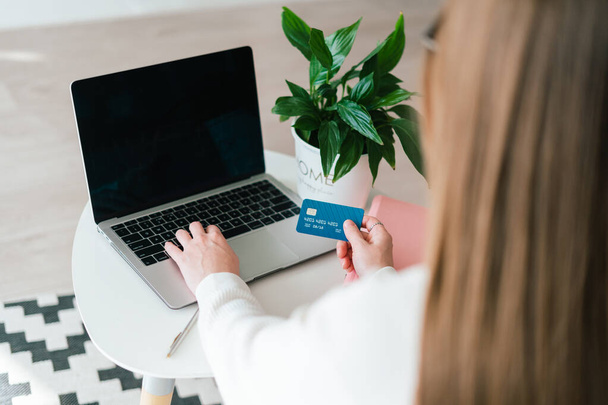 Młoda kobieta siedząca za biurkiem i używająca karty debetowej do zakupów internetowych na laptopie. Blank kopia przestrzeń makieta laptop ekran z kwiatem w tle. - Zdjęcie, obraz