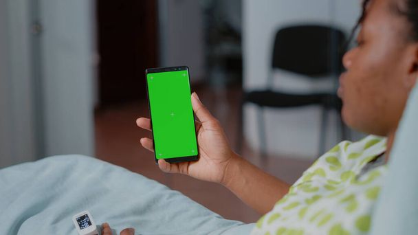 Крупним планом пацієнт тримає смартфон із зеленим екраном у лікарняному відділенні. Мобільний телефон з ізольованим фоном і макетним шаблоном з клавішею хромосоми на екрані. Людина з телефоном
 - Фото, зображення