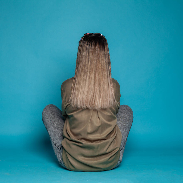 Female back on blue studio background. Young woman sitting on floor - Foto, Imagem