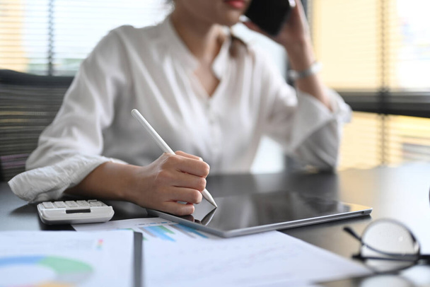 Erschossene Geschäftsfrau führt Handygespräche und nutzt digitales Tablet an ihrem Arbeitsplatz. - Foto, Bild