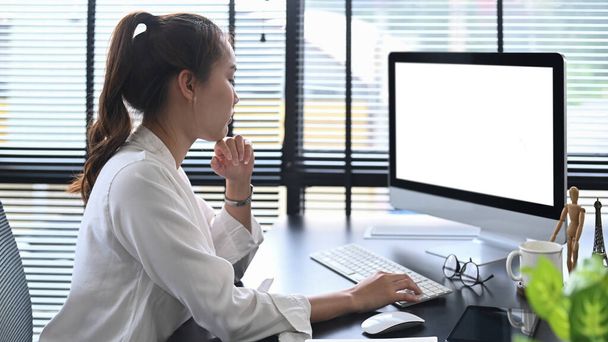 Συγκεντρωμένη ασιάτισσα επιχειρηματίας που διαβάζει επιχειρηματικό email, βλέποντας σε απευθείας σύνδεση webinar στο χώρο εργασίας. - Φωτογραφία, εικόνα