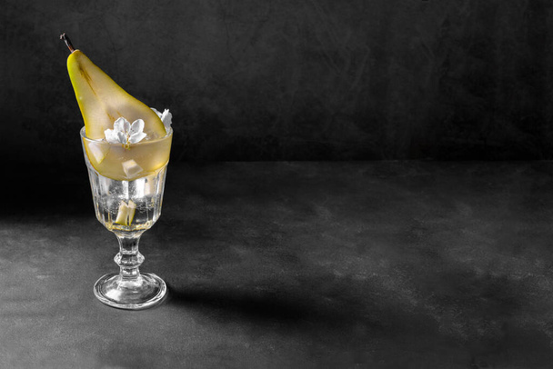 Cóctel de pera en un vaso decorado con fruta fresca y flores sobre fondo gris oscuro. Bebida fría de la pera del verano limonada con el hielo en la tabla, bebida espumosa del postre de la escaramuza con con el espacio de la copia - Foto, imagen