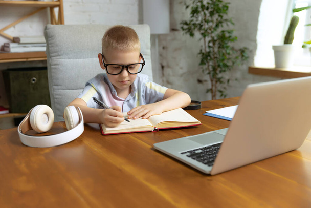 Remote learning. One cute little boy, school age kid listening online lesson, using laptop at home interior. On-line education, childhood, people, homework and school concept. Looks happy, calm - Foto, afbeelding
