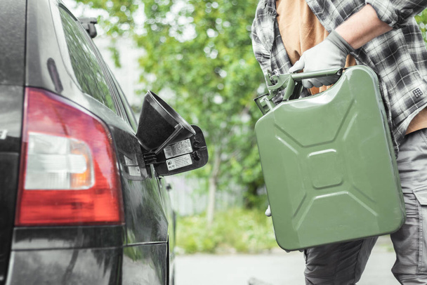 Bir adam bir teneke kutudan bir arabanın tankına benzin döker. Benzin dolu yeşil bir Jerrycan. Seyahat ederken yakıt sıkıntısı. - Fotoğraf, Görsel
