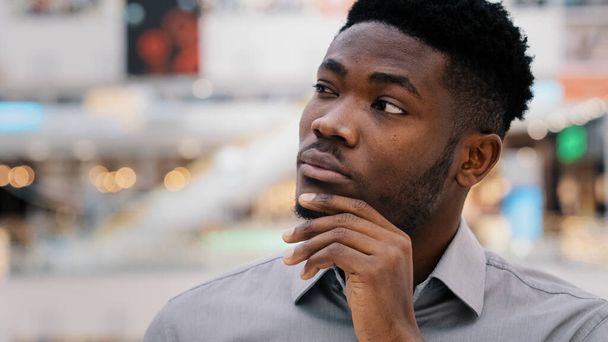 Close-up puzzled concentrated pensive serious african american young man looking away keeps hand on chin thinks solves problem comes up with new opportunities idea startup dreaming plunged thoughts - Фото, изображение