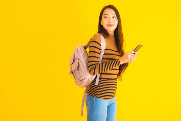 Portret pięknej młodej azjatyckiej kobiety z torbą korzystać inteligentny telefon komórkowy lub telefon komórkowy w wielu akcji na żółtym odizolowanym tle - Zdjęcie, obraz