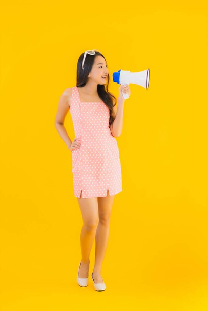 Güzel bir Asyalı kadın, sarı izole edilmiş arka planda megafonla yüksek sesle konuşur. - Fotoğraf, Görsel
