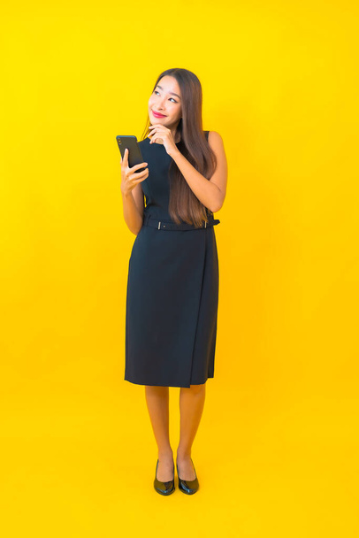 Portrait beautiful young asian business woman with coffee cup and smart mobile phone on yellow background - Fotoğraf, Görsel