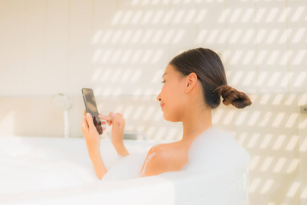 Πορτρέτο νεαρή Ασιάτισσα γυναίκα χρησιμοποιώντας έξυπνο κινητό τηλέφωνο στην μπανιέρα για την έννοια spa - Φωτογραφία, εικόνα