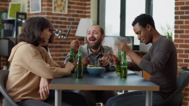 Boldog barátok élvezik az összejövetelt sörrel és nasival, beszélgetnek és nevetnek együtt. Egy csapat pozitív ember sörözik és viccelődik a nappaliban. Szabadidős tevékenység. - Felvétel, videó