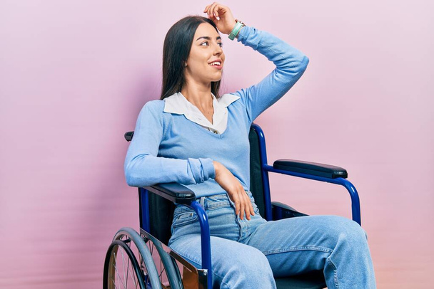 Beautiful woman with blue eyes sitting on wheelchair smiling confident touching hair with hand up gesture, posing attractive and fashionable  - Zdjęcie, obraz