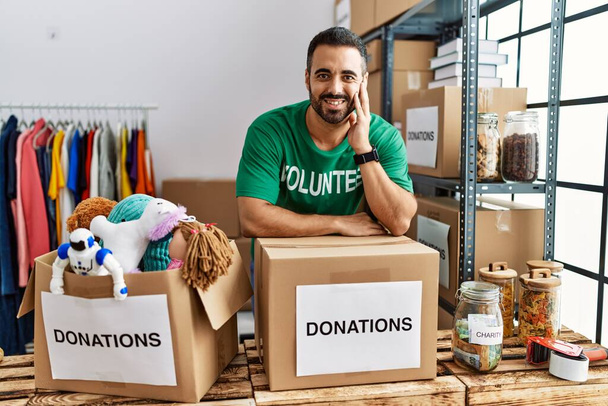 Fiatal spanyol férfi önkéntes egyenruhát visel, adománygyűjtő dobozra támaszkodik a jótékonysági központban. - Fotó, kép