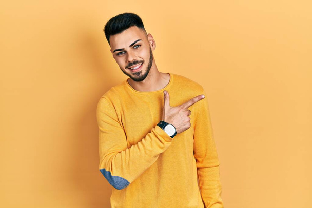 Young hispanic man with beard wearing casual winter sweater smiling cheerful pointing with hand and finger up to the side  - Photo, Image