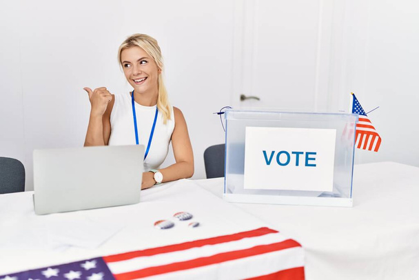 Jonge blanke vrouw bij de Amerikaanse politieke campagne verkiezing glimlachend met een vrolijk gezicht en wijzend naar de zijkant met duim omhoog.  - Foto, afbeelding