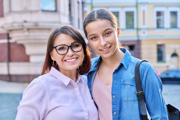 Portrait of happy mom and teenage daughter looking at camera outdoor on city street. Smiling mother and teen girl together. Family, two generations, lifestyle, leisure, people concept - Fotoğraf, Görsel
